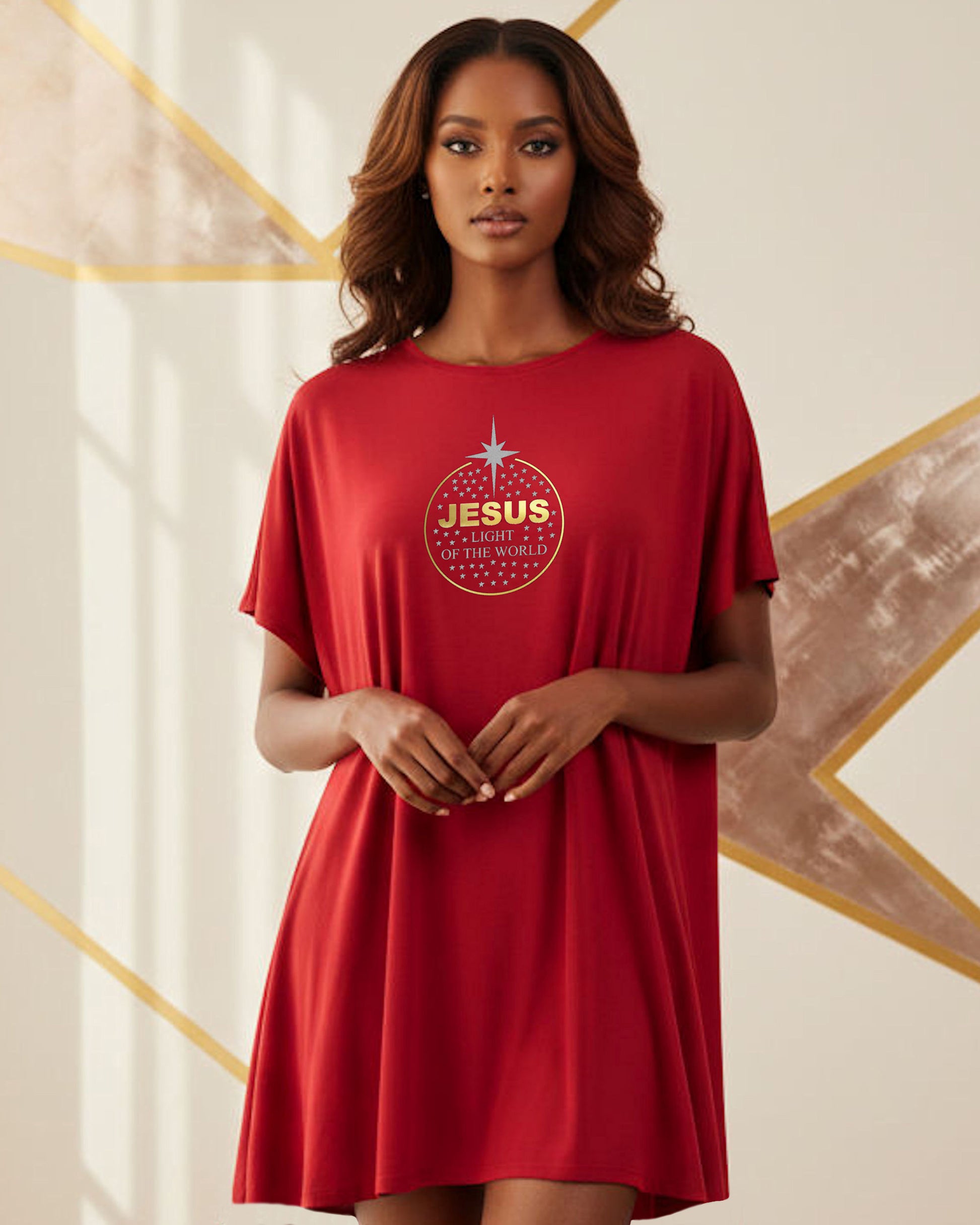 A woman indoors wearing a red t-shirt dress with a gold text logo "Jesus" and silver text, "light of the world" within a gold circle containing silver stars.
