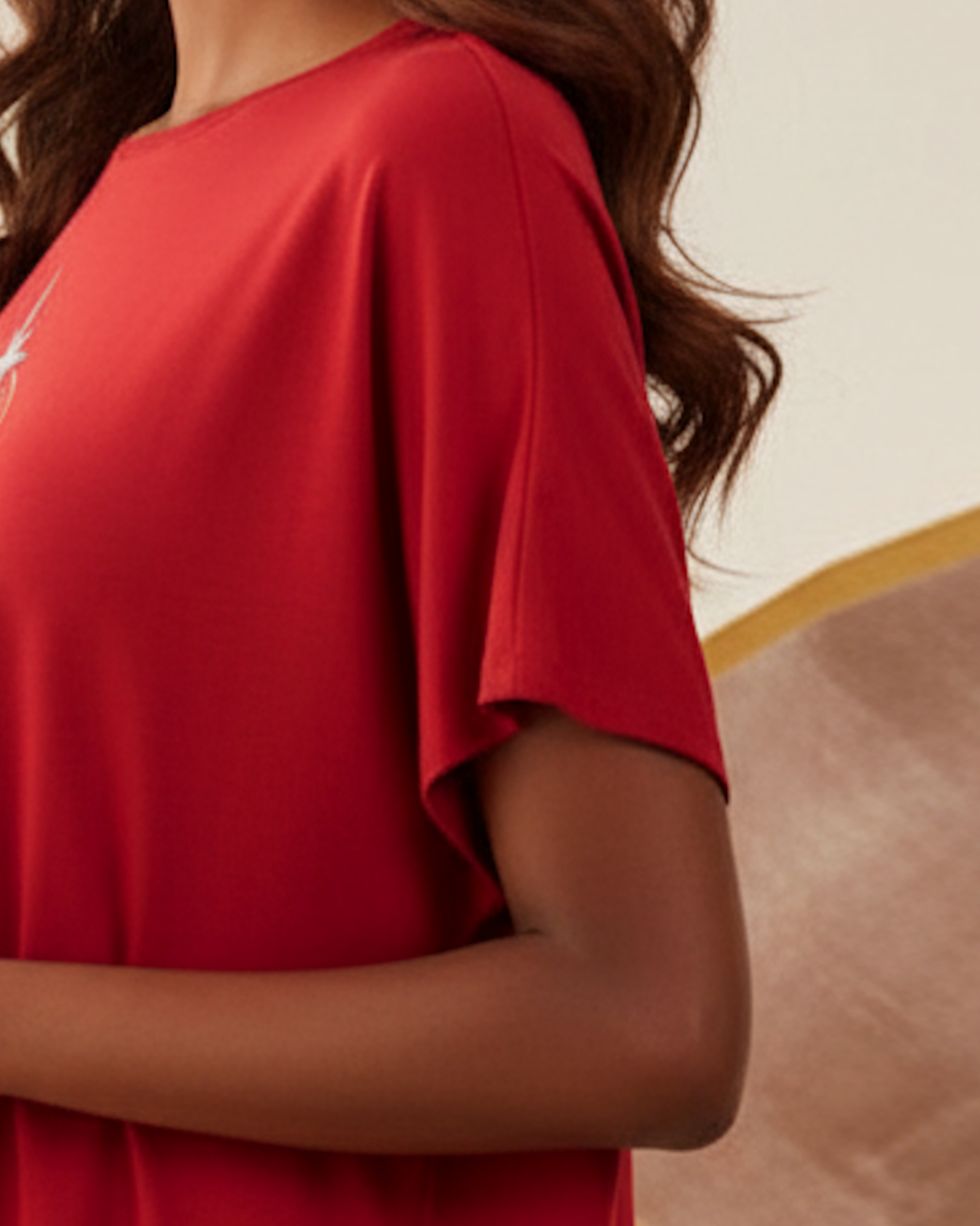 Closeup of the sleeve of a red t-shirt worn by a woman against a decorative wallpaper background.