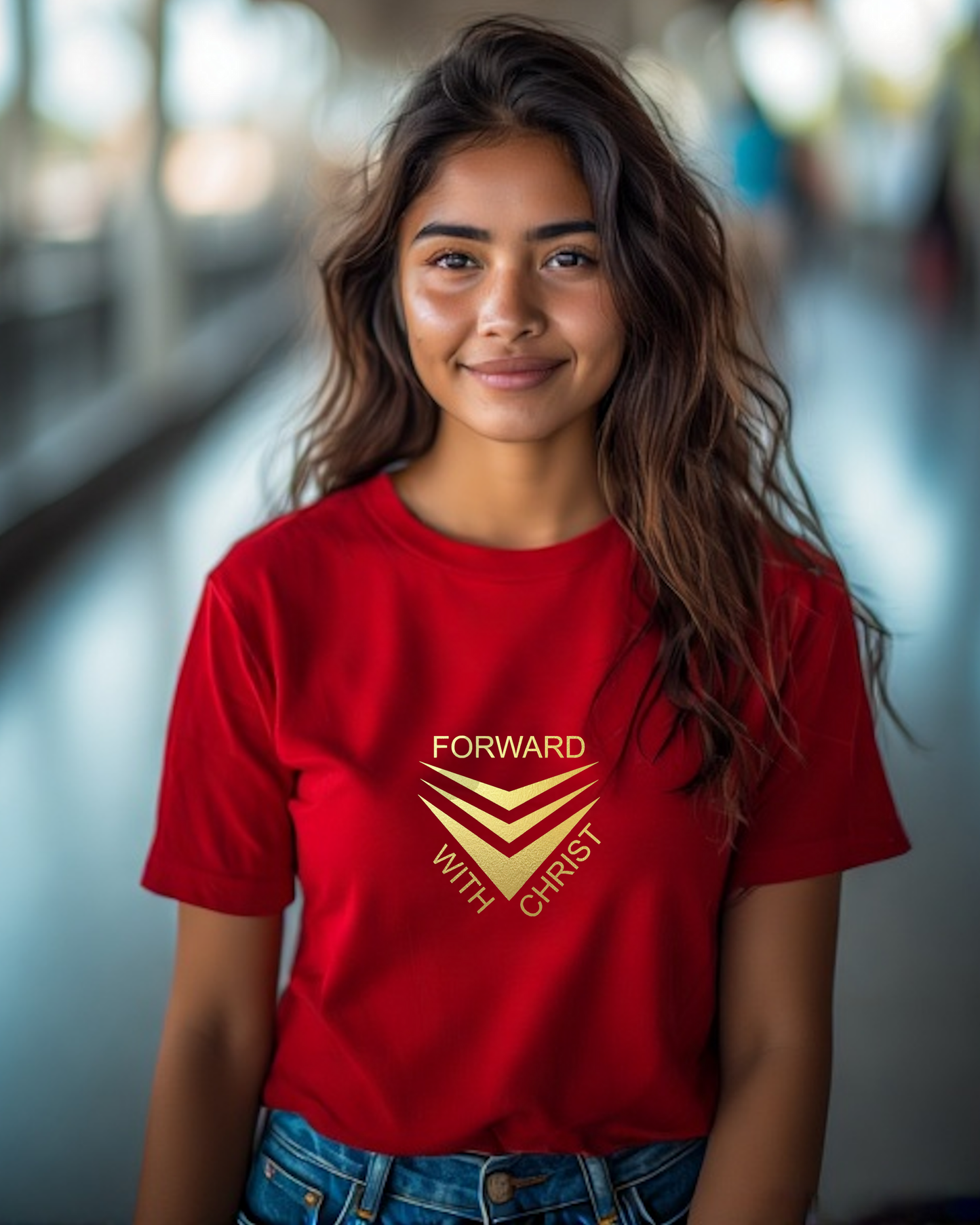 A woman standing in a street wearing a red short sleeve t-shirt that has a gold logo with the words "FORWARD WITH CHRIST" around 3 downward pointing chevrons.