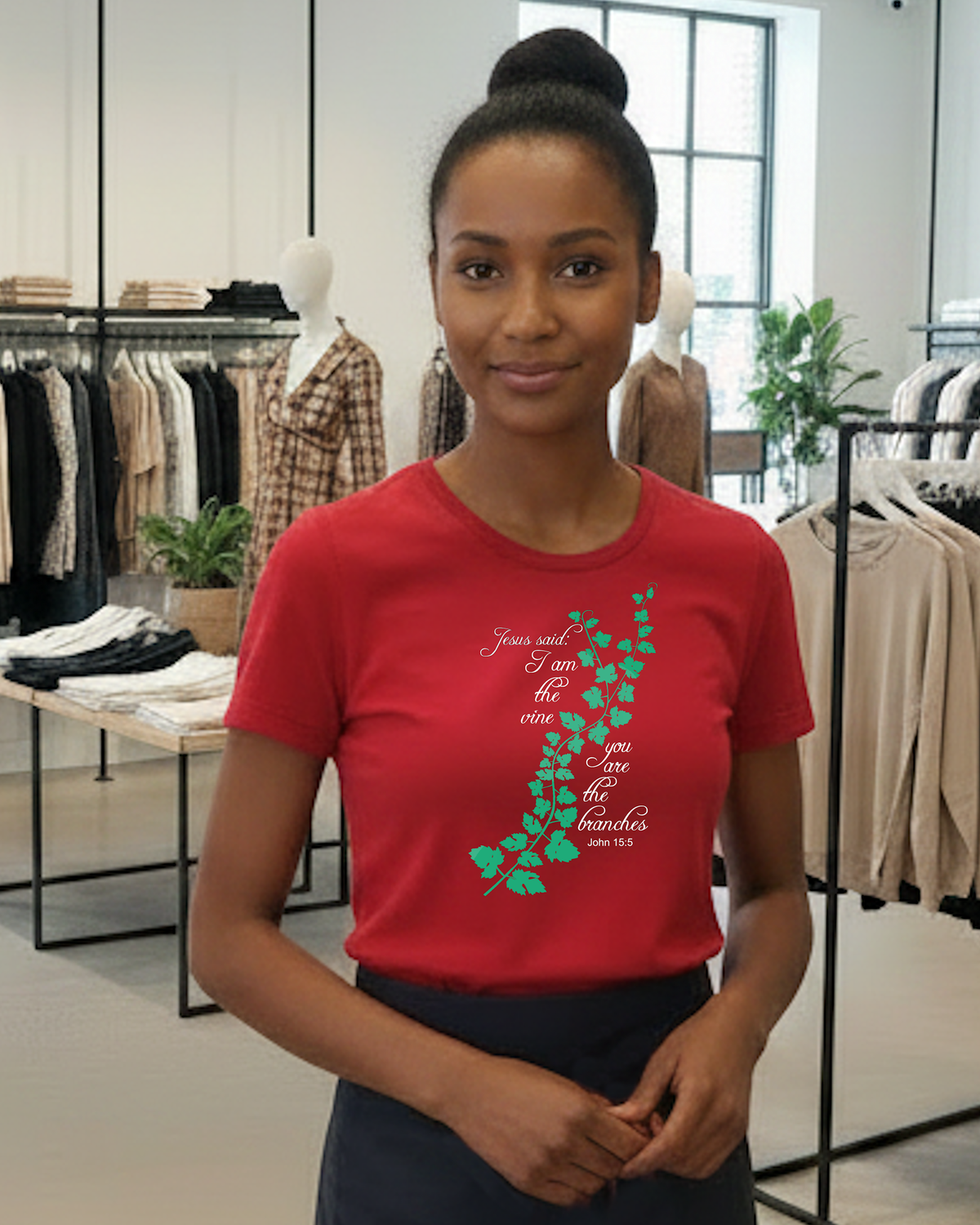 A woman wearing a red graphic t-shirt with a green vine design and white cursive text 'Jesus said I am the vine you are the branches', standing inside a clothing store.