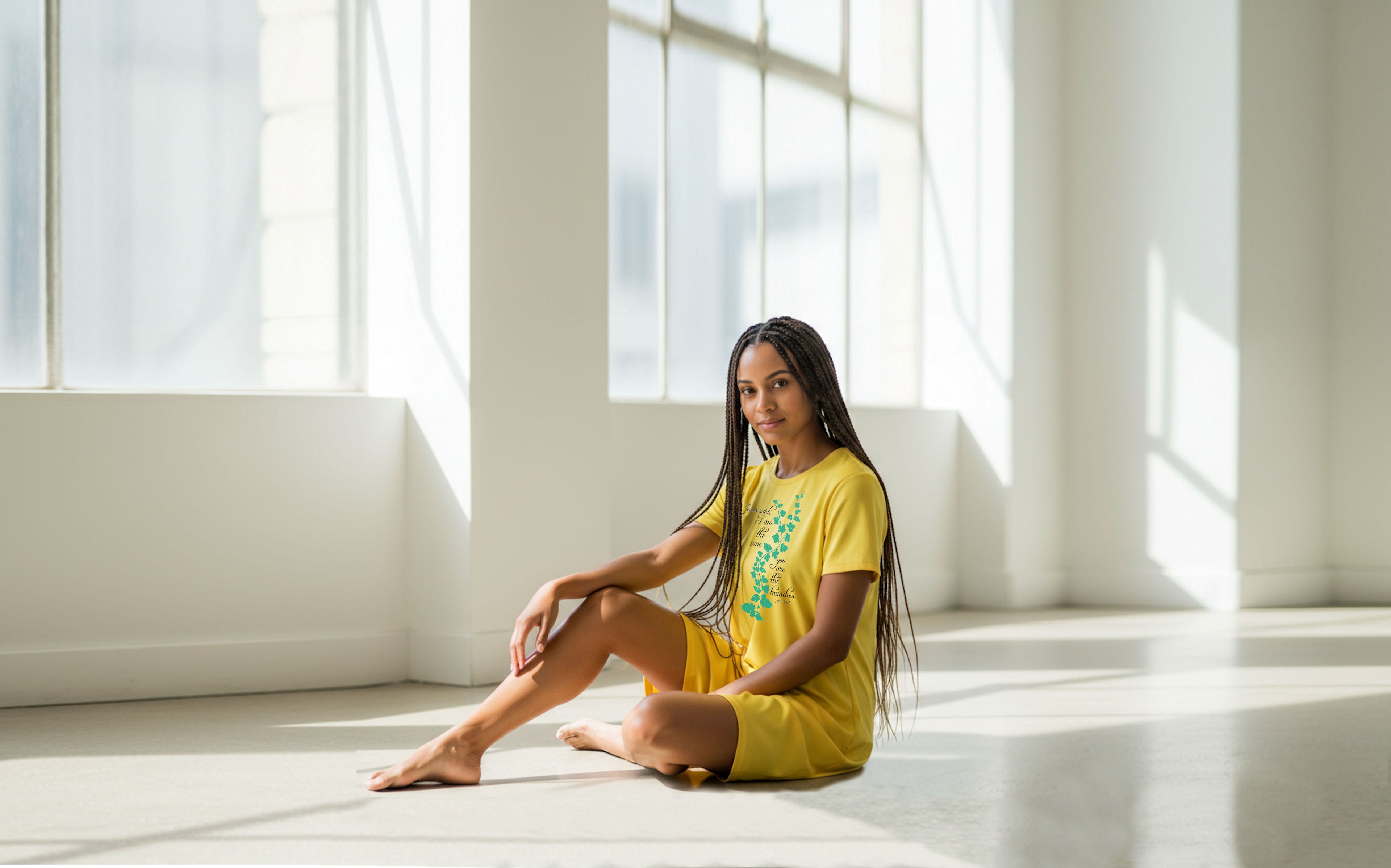 Woman in yellow t-shirt dress outfit sitting on a white floor with large windows in the background
