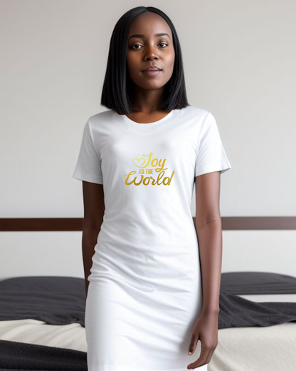 A woman standing in a bedroom wearing a white Heavenly Dreamwear t-shirt dress with a gold "Joy to the World" logo printed on the front.