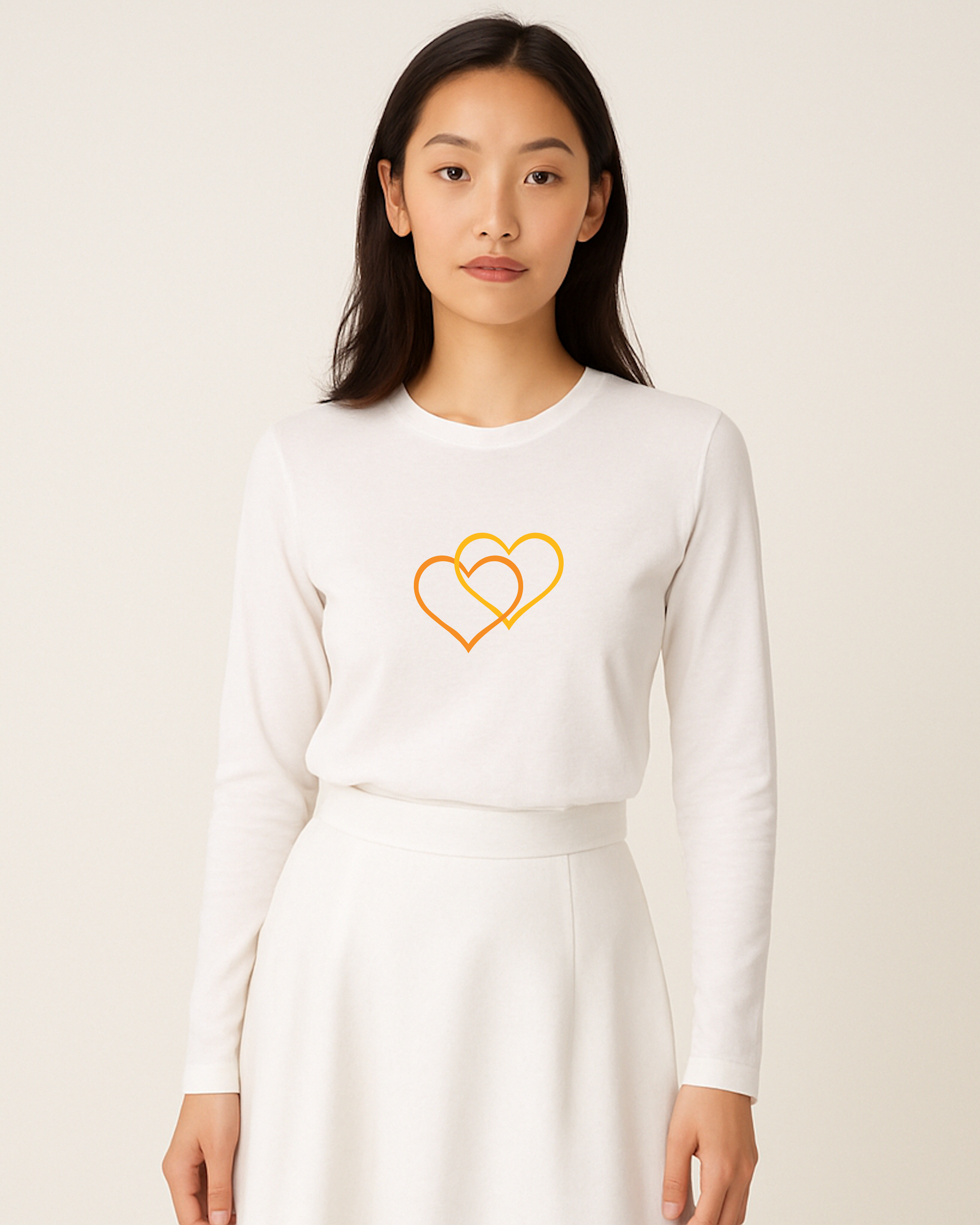 A woman wearing a white long sleeve T-shirt with a dual orange/yellow inter-twinned heart design on a plain background