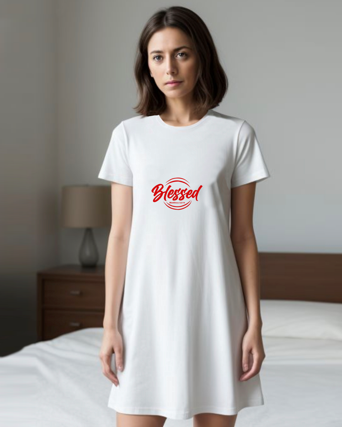 Woman wearing a white t-shirt dress with 'Blessed' printed on it in a bedroom setting.