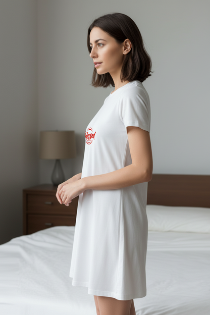 Woman wearing a white t-shirt dress in a bedroom setting.