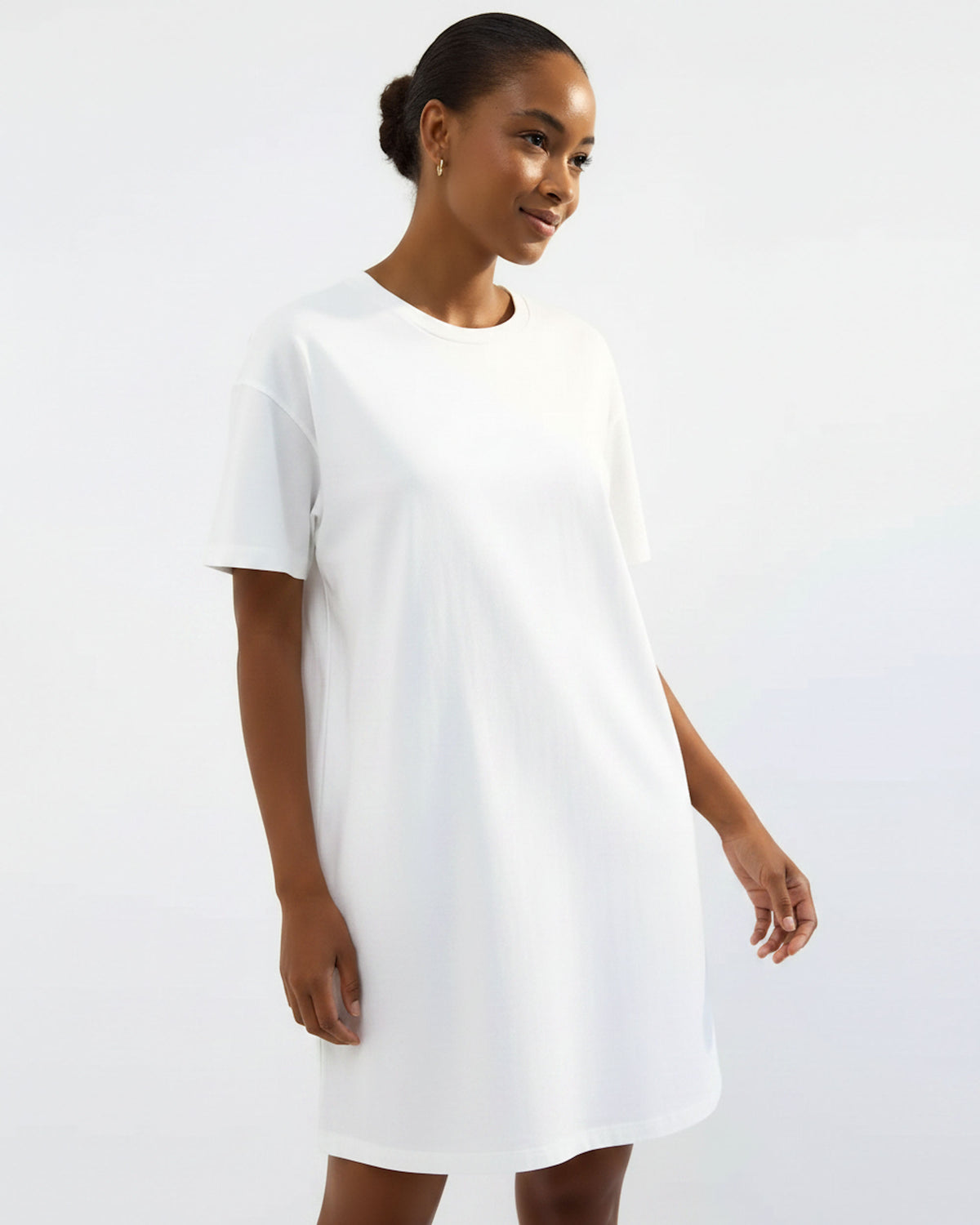 A woman wearing a plain white short-sleeve t-shirt dress, standing against a light gray studio background.