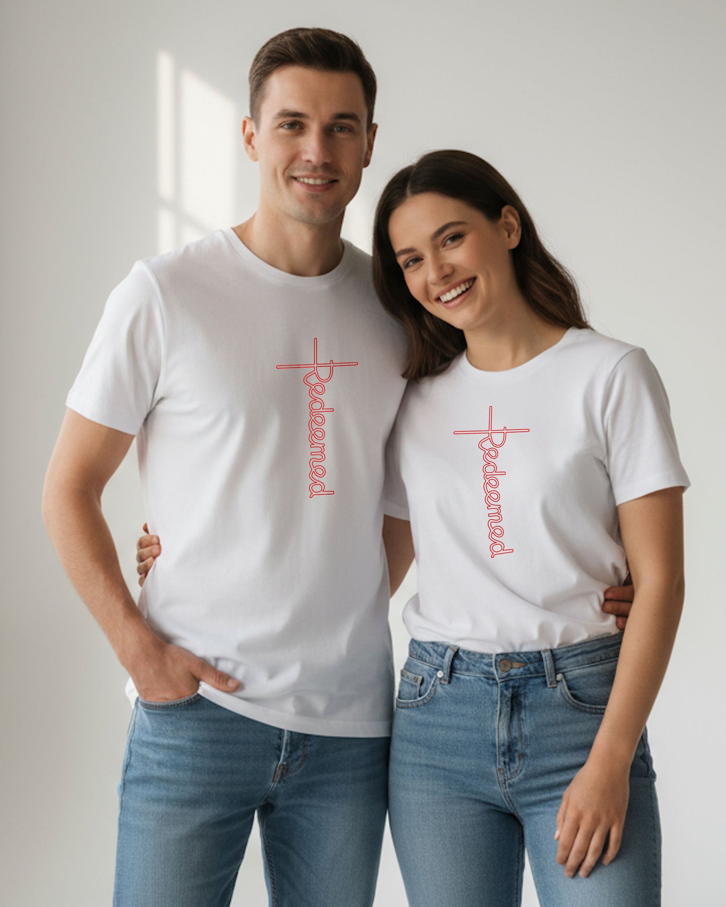 A man and a woman wearing white t-shirts with an elaborate red 'Redeemed' logo printed on the front, designed by Heavenly Dreamwear.