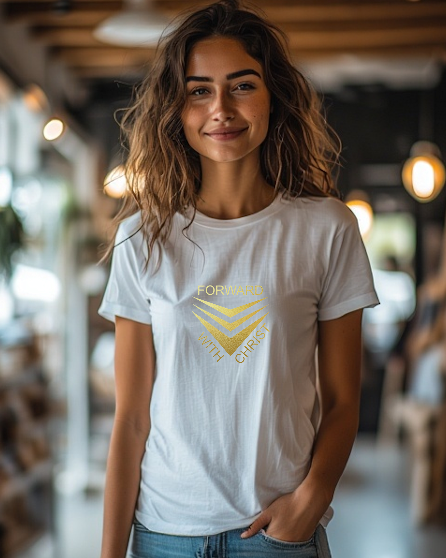 A woman standing in a cafe wearing a white short sleeve t-shirt that has a gold logo with the words "FORWARD WITH CHRIST" around 3 downward pointing chevrons.