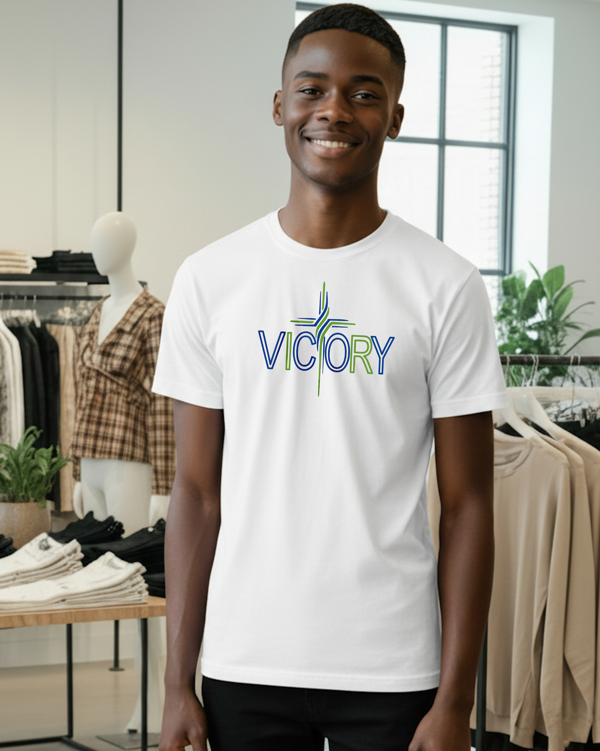 A smiling man wearing a white crewneck t-shirt with a colorful 'VICTORY' graphic on the chest, standing inside a clothing boutique.