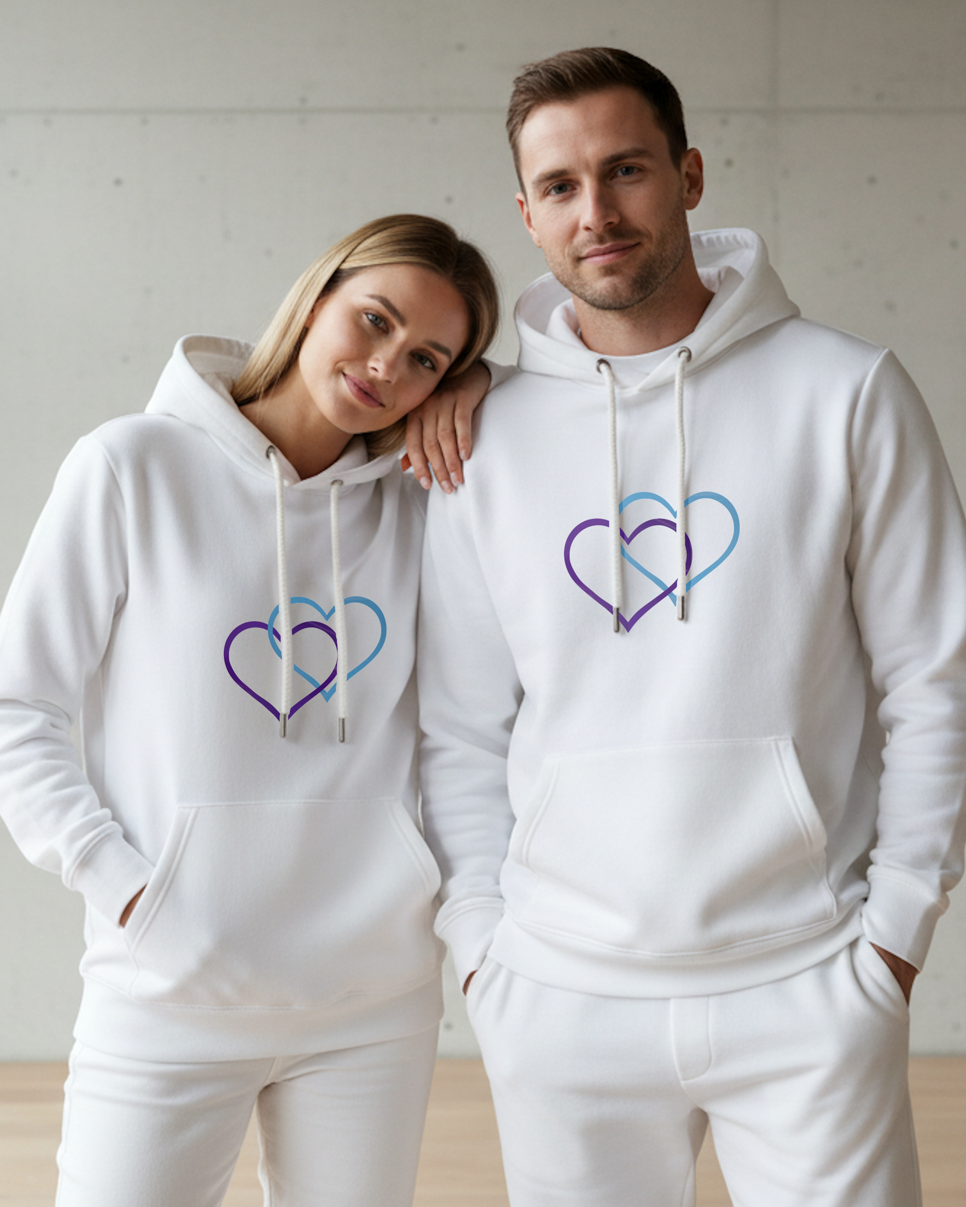 A couple wearing white hoodies with a dual purple and cyan heart design, standing close together against a plain background.