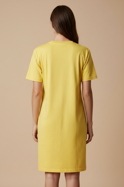 A woman viewed from the back wearing a short-sleeve yellow t-shirt dress, standing against a plain beige studio background.