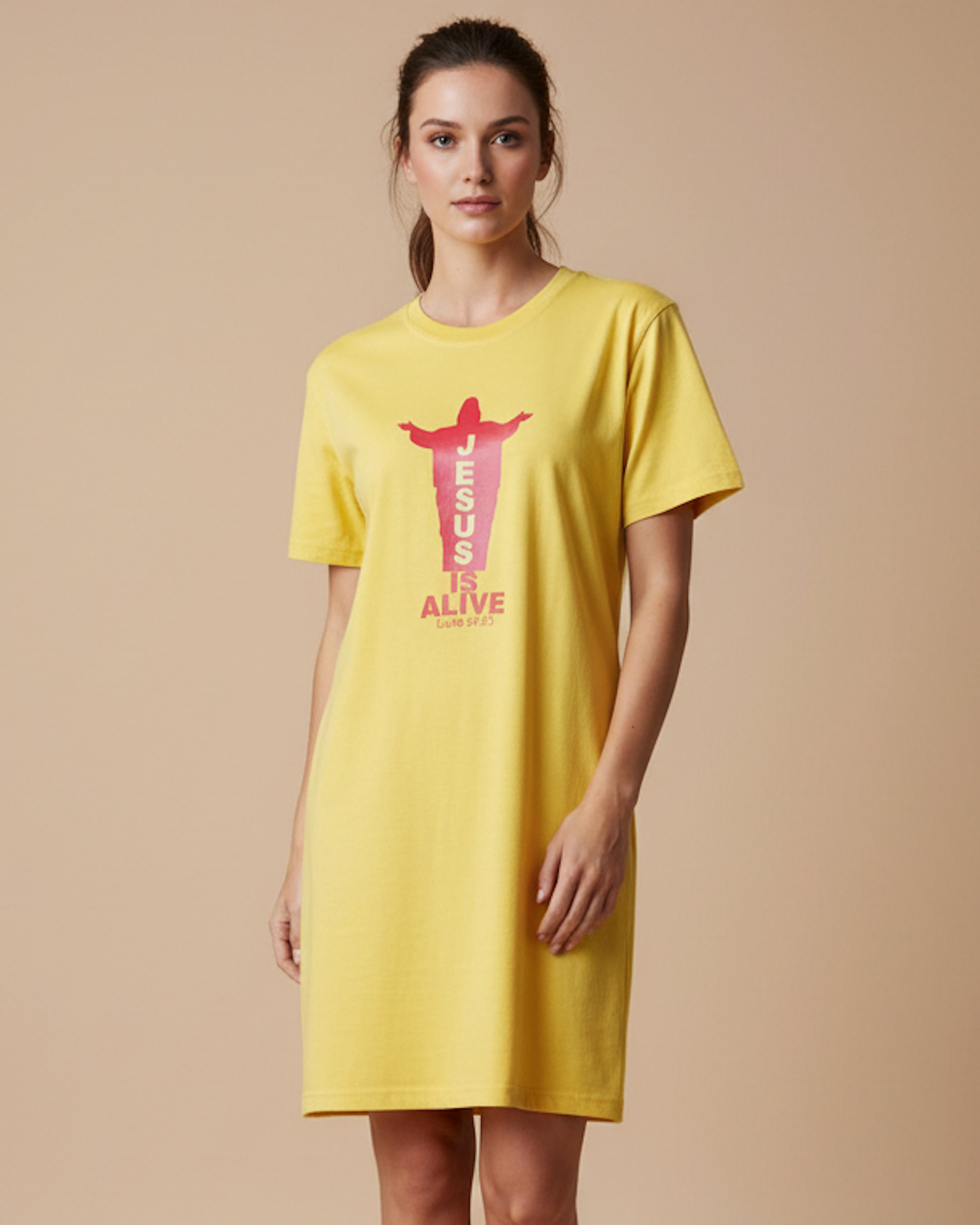A woman modeling a bright yellow t-shirt nightdress with a red graphic of Jesus raising his hands and the text 'JESUS IS ALIVE' on the front, set against a solid beige background.