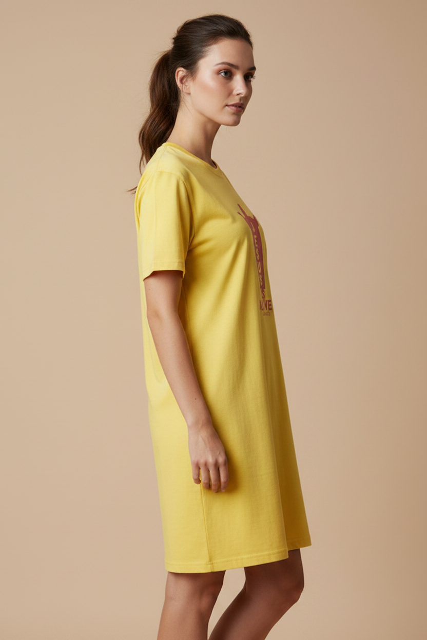 A woman modeling a bright yellow short-sleeve t-shirt dress with a graphic print on the front, set against a solid beige studio background.