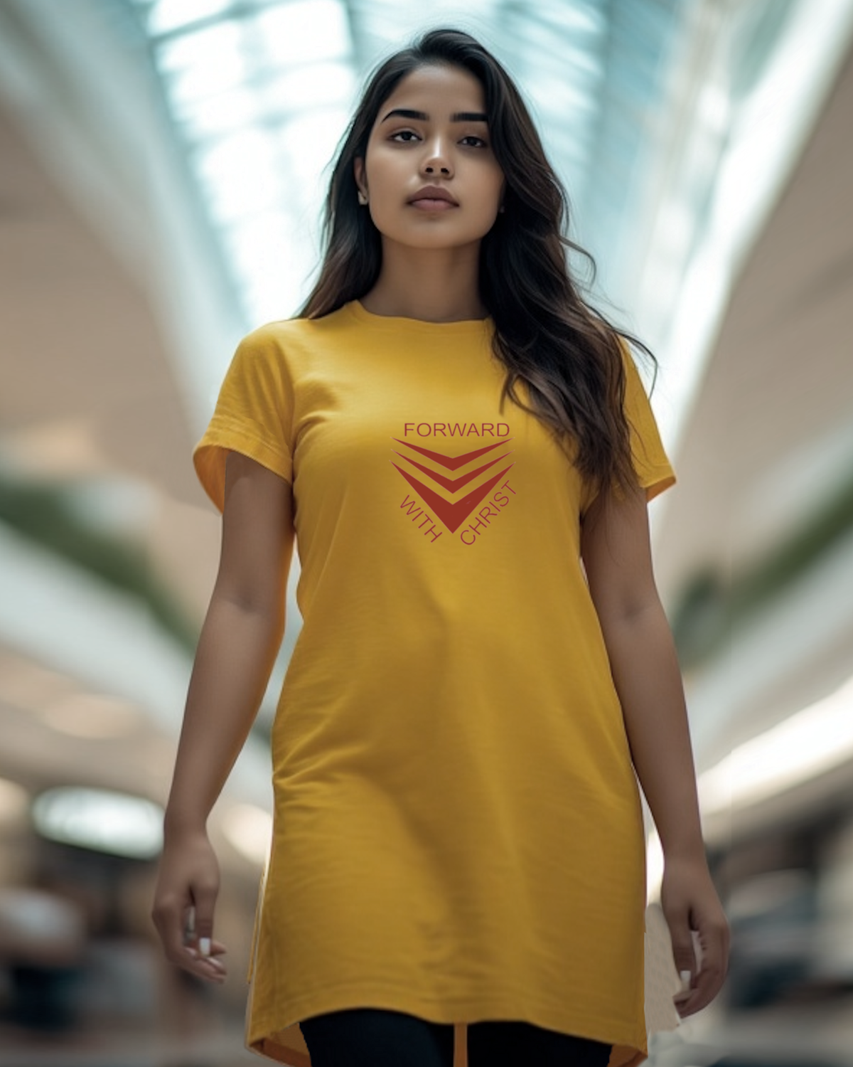 A woman standing in a mall wearing a yellow Heavenly Dreamwear t-shirt dress with a red logo made up of  3 chevrons surrounded by the text, "Forward With Christ".