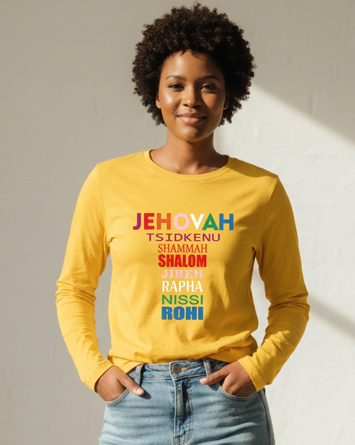 Woman wearing a yellow long sleeve t-shirt with a multi-colored text logo printed on the front against a white wall