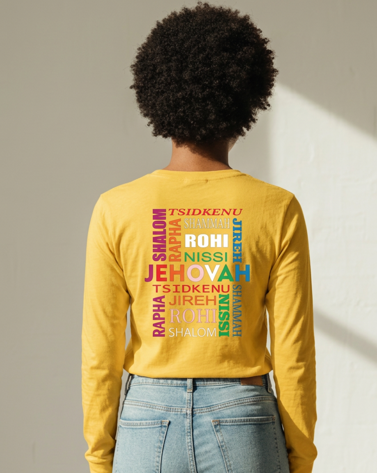 Woman wearing a yellow short sleeve t-shirt with a multi-colored text logo printed on the back against a white wall