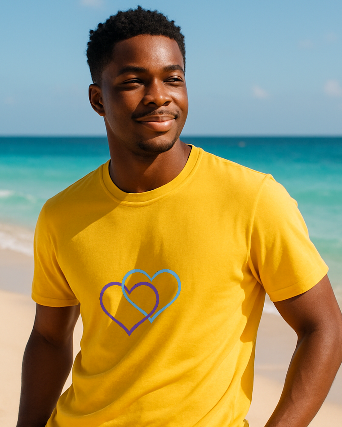 A man on a beach wearing a yellow t-shirt with a Heavenly Dreamwear logo comprised of a purple and blue inter-twinned hearts.