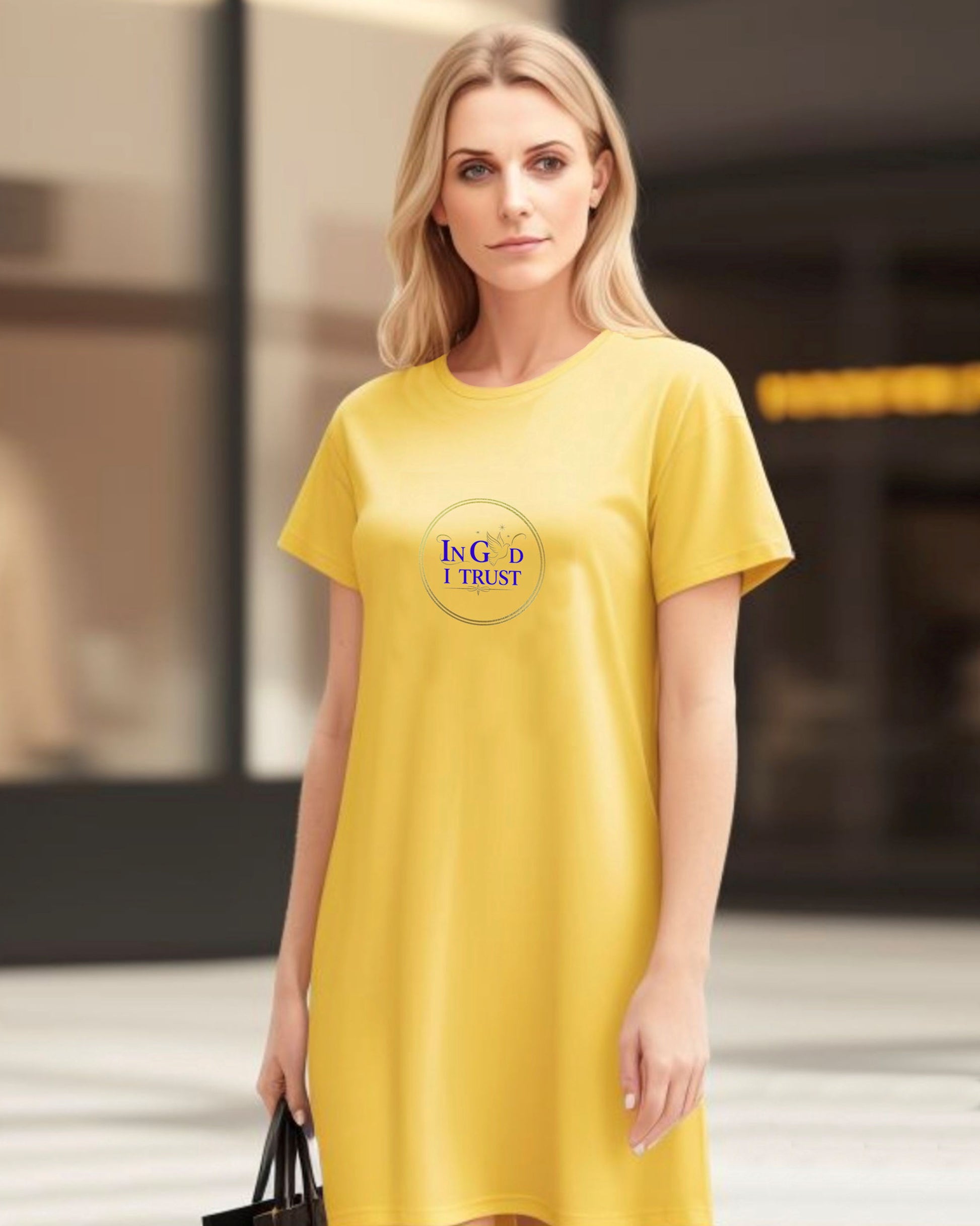 Woman wearing a yellow t-shirt dress with a gold ring logo and purple text, 'In God I Trust', in an urban setting.