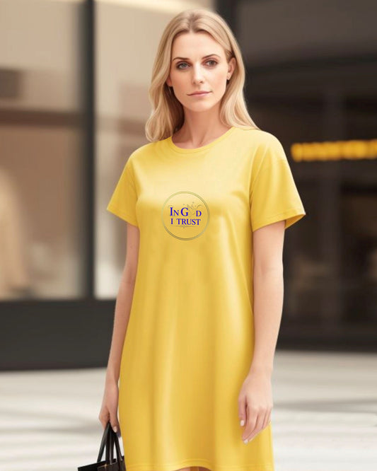 Woman wearing a yellow t-shirt dress with a gold ring logo and purple text, 'In God I Trust', in an urban setting.