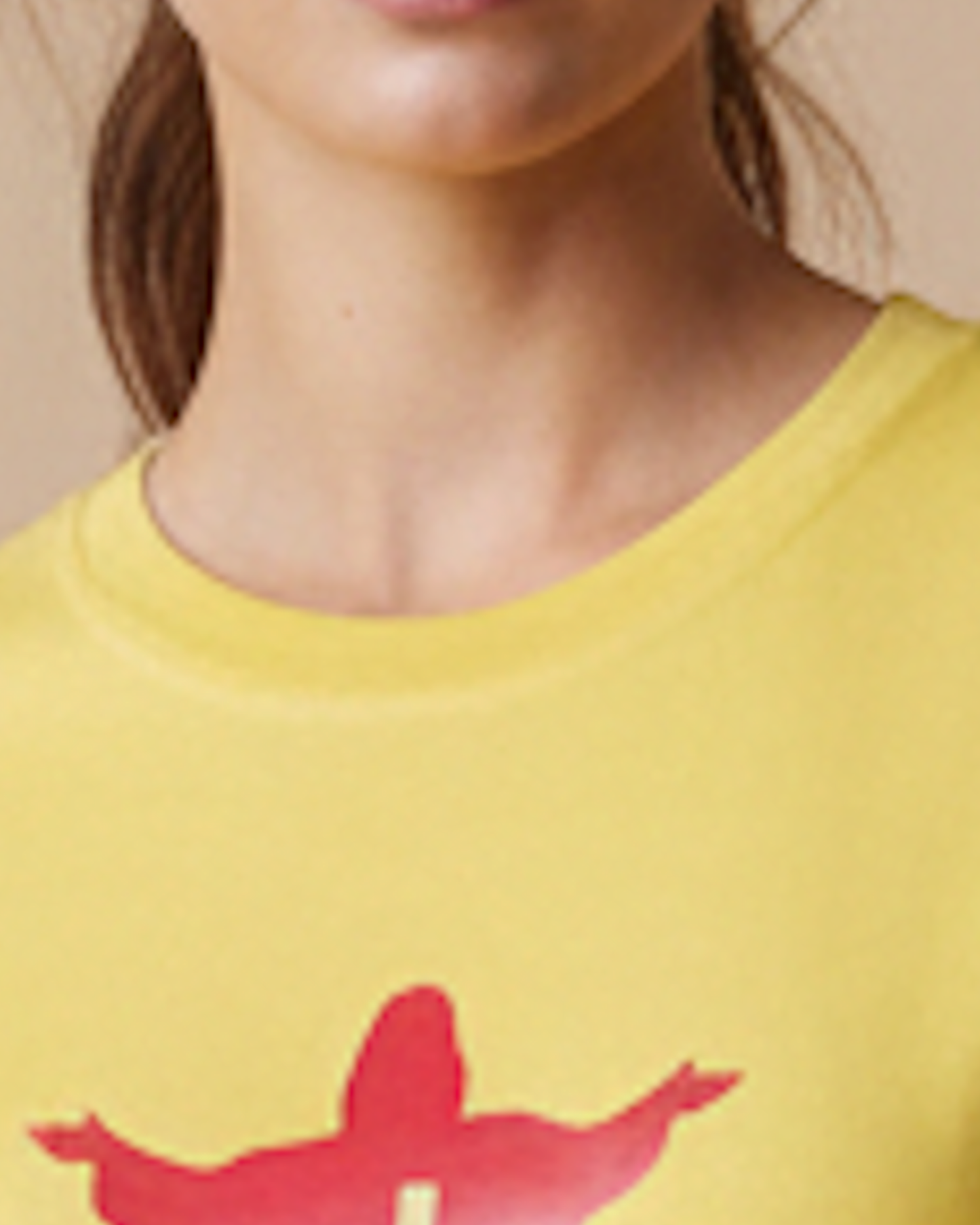 Close-up of a woman wearing a bright yellow crew-neck T-shirt with a red graphic print on the chest, against a plain beige background.