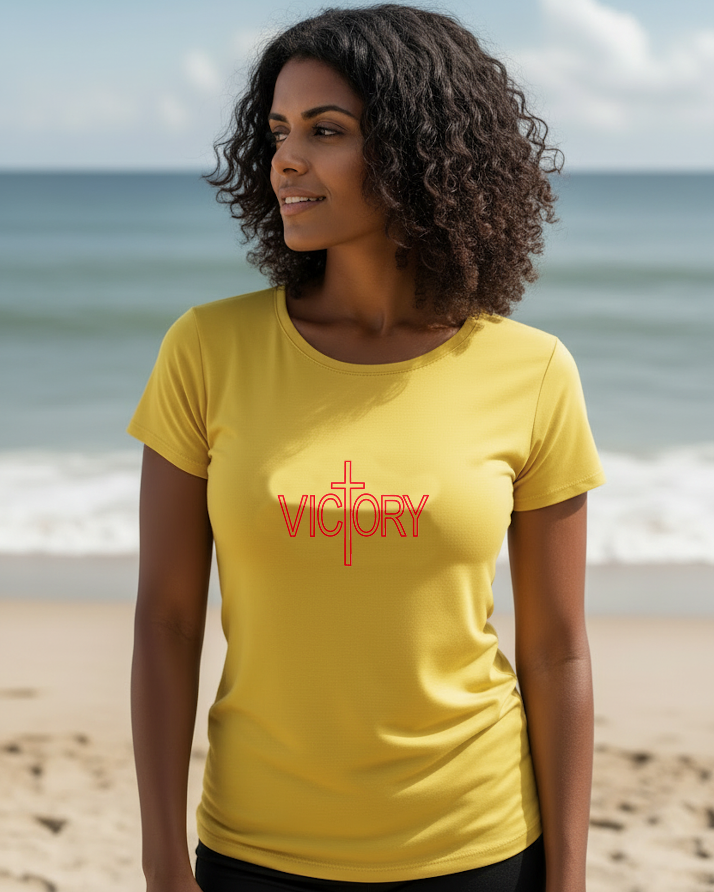 A woman wearing a yellow t-shirt with a red "Victory" logo printed on the front, standing on a beach.