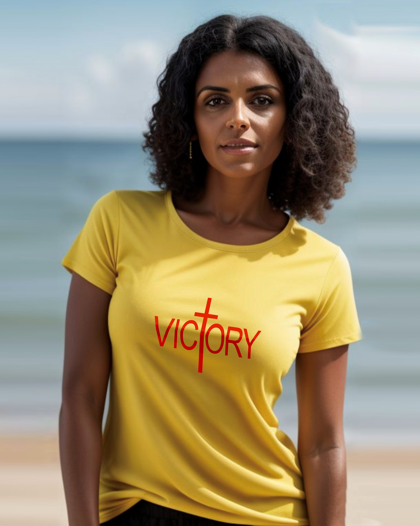 A woman wearing a yellow t-shirt with a white Heavenly Dreamwear "Victory" logo printed on the front, standing on a beach.